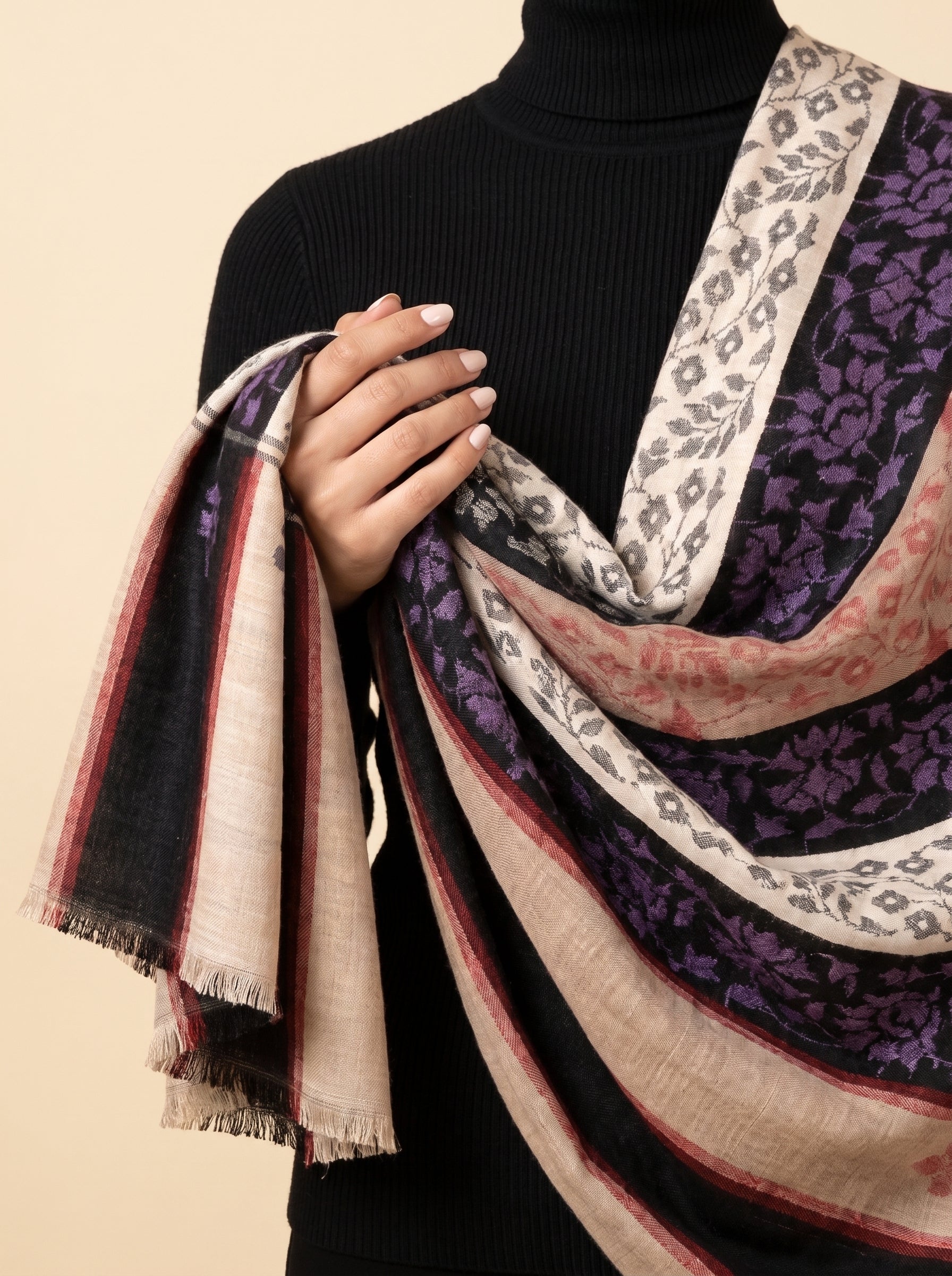 A close-up of a person wearing a black ribbed turtleneck sweater and draping a large patterned scarf. The scarf features multiple colors and patterns including purple floral motifs, gray leopard print, and stripes in beige, black, and red.